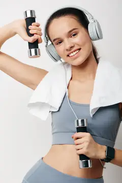 Улыбающаяся девушка с гантелями и в наушниках на тренировке