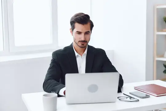 Молодой мужчина в костюме работает за ноутбуком в светлом офисе