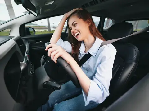 Смеющаяся рыжеволосая девушка за рулём автомобиля
