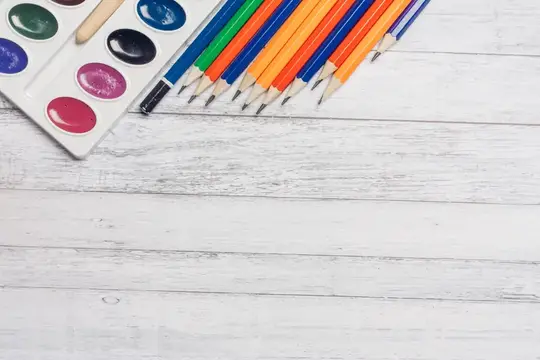Акварельные краски и цветные карандаши на белом деревянном столе