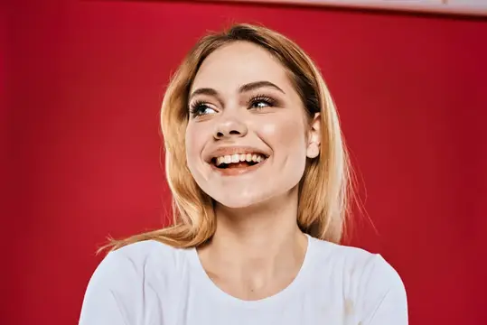 Светловолосая женщина искренне улыбается на красном фоне
