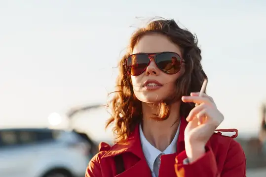 Молодая женщина в красном пальто и солнцезащитных очках на закате