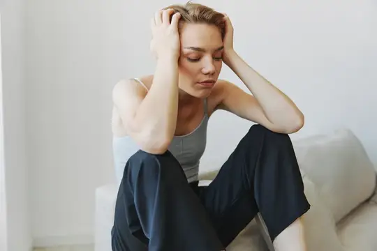 Уставшая женщина сидит на диване и держится за голову