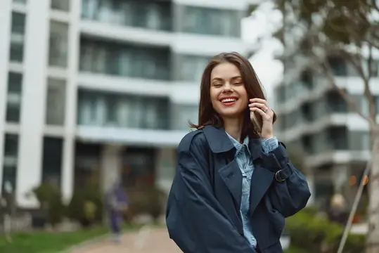 Улыбающаяся девушка в плаще разговаривает по телефону на городской улице