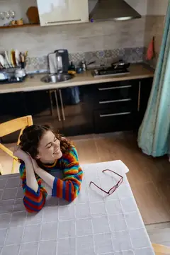 Игривая сцена: улыбающаяся женщина дома, кухонная обстановка, яркий свитер, детали на столе, естественные цвета, комфортный образ жизни, непринуждённое настроение, домашний момент