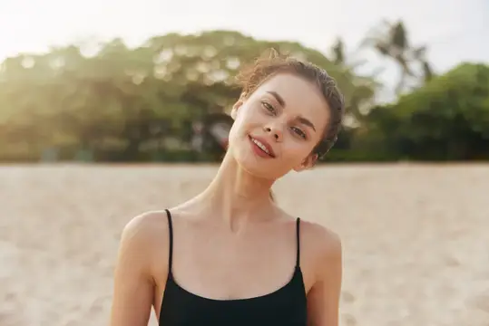 Улыбающаяся темноволосая девушка на песчаном пляже в тёплом вечернем свете