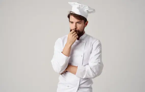 Задумчивый бородатый повар в белом колпаке на сером фоне