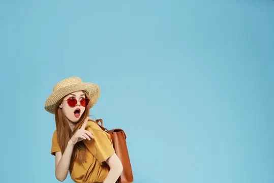 Удивлённая девушка в соломенной шляпе и красных очках с рюкзаком