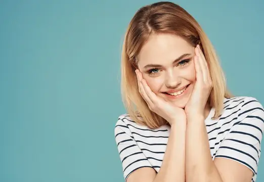 Улыбающаяся блондинка с ладонями у лица на бирюзовом фоне