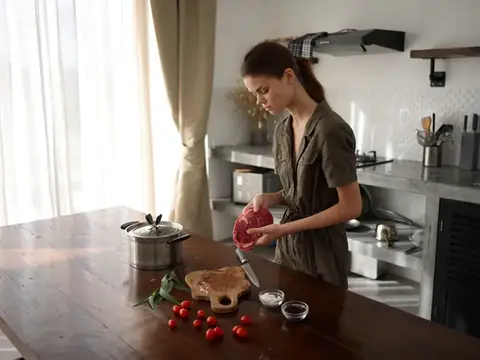 Женщина на кухне готовит ужин из мяса, овощей и специй на деревянном столе на фоне стильной кухни