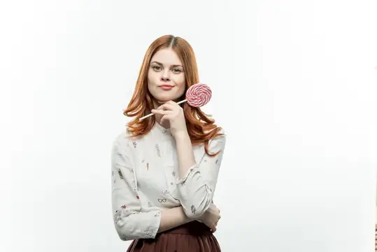 Рыжеволосая девушка с леденцом на палочке у лица на белом фоне