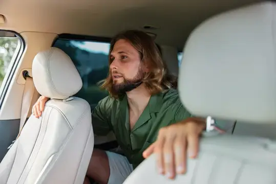 Бородатый мужчина с длинными волосами оборачивается на заднее сиденье автомобиля