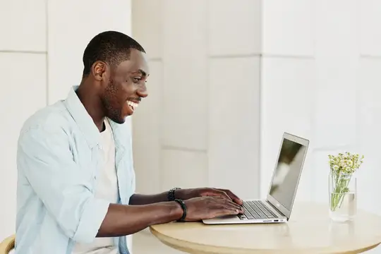 Улыбающийся темнокожий мужчина работает за ноутбуком за светлым столом