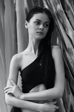 Элегантная женщина в стильном топе на одно плечо грациозно позирует на фоне дерева на черно-белой фотографии