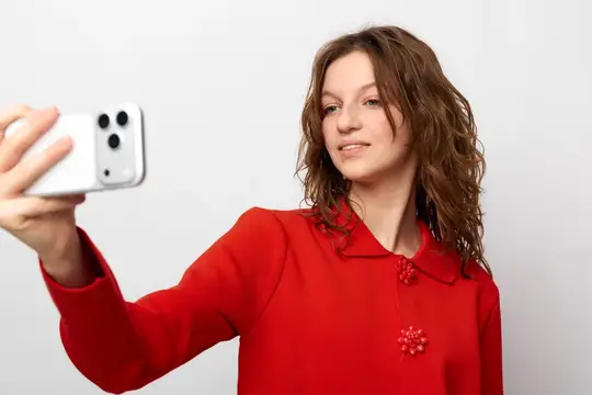 Улыбающаяся женщина в красном свитере держит смартфон для селфи на белом фоне