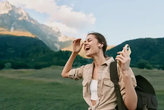 Смеющаяся девушка с рюкзаком и телефоном на фоне гор