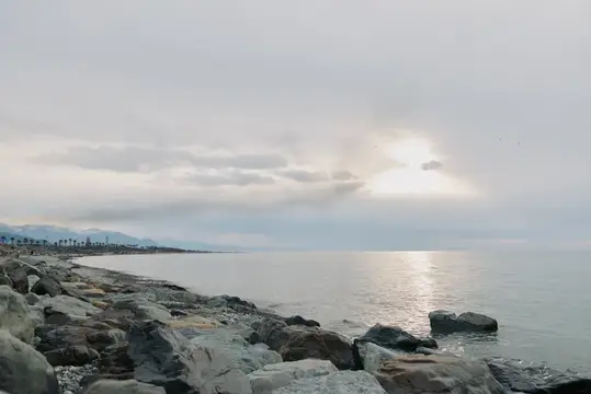 Каменистый берег моря под пасмурным небом с проблеском солнца
