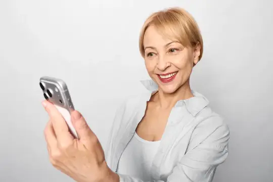Улыбающаяся блондинка со смартфоном в руках на светлом фоне