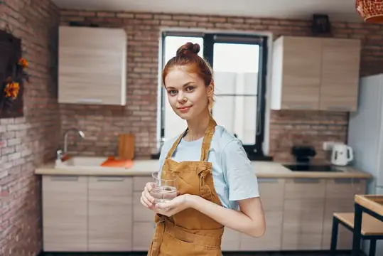 Весёлая женщина в фартуке на кухне, занимающаяся домашними делами в современном стиле