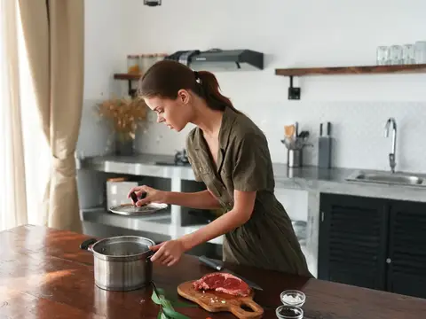 Молодая женщина готовит мясо на кухне у окна