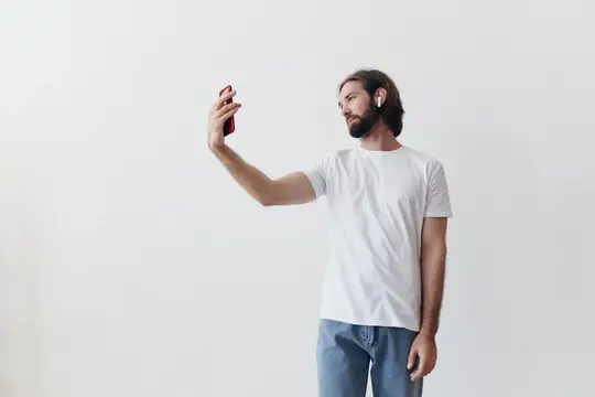 Бородатый мужчина в белой футболке делает селфи на смартфон