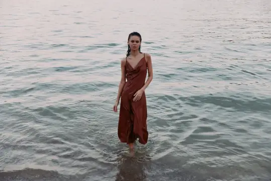 Молодая женщина в коричневом платье стоит в воде на закате