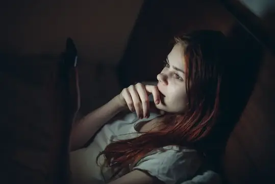 Рыжеволосая девушка лежит в темноте и смотрит в планшет