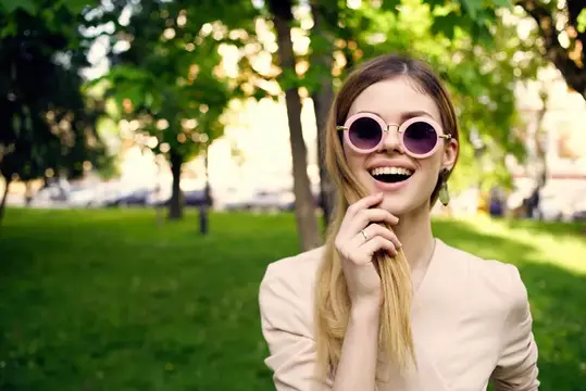 Смеющаяся девушка в круглых солнцезащитных очках в летнем парке