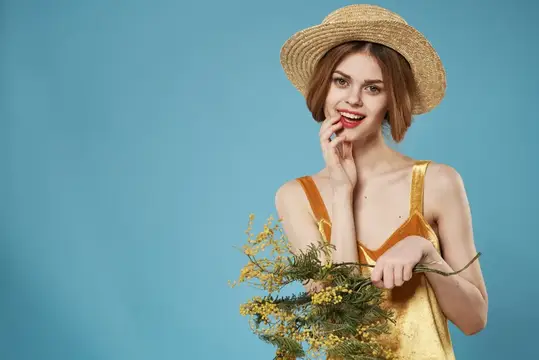 Рыжеволосая девушка в соломенной шляпе с веточками мимозы на голубом фоне