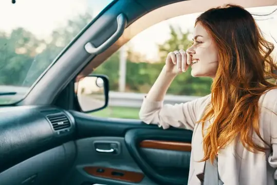 Рыжеволосая девушка смеётся, высунувшись из окна автомобиля