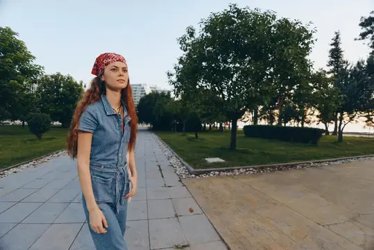 Женщина в стиле лайфстайл, одетая в современный бохо-вестерн деним в стиле стрит, уверенно идет по городскому тротуару в окружении деревьев