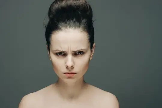 Симпатичная женщина с обнаженными плечами, недовольным взглядом и чистой кожей на сером фоне