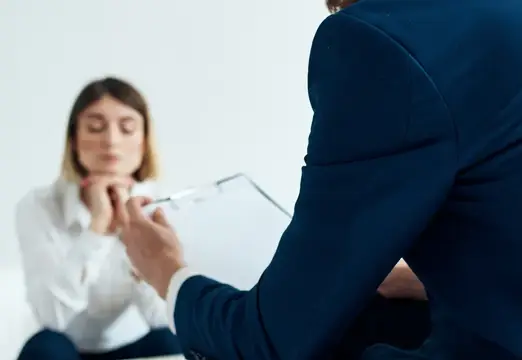 Бизнесмен в синей куртке и женщина на заднем плане за столом