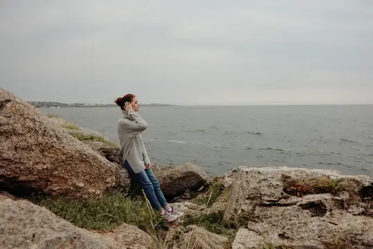 Молодая женщина отдыхает на камнях у моря в пасмурный день