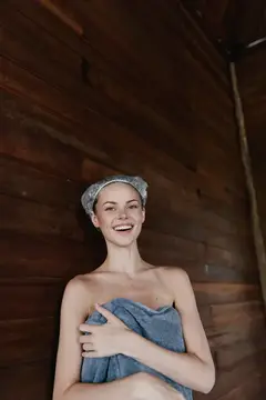 Улыбающаяся девушка в шапочке для душа прикрывает полотенцем грудь