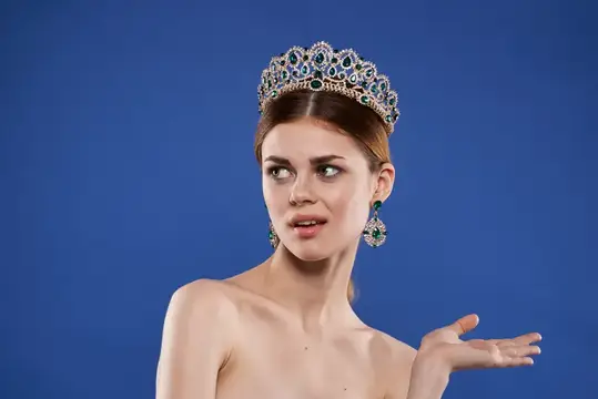 Молодая женщина в роскошной короне с изумрудами на синем фоне