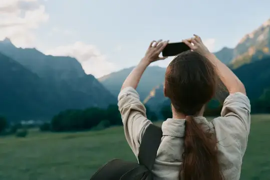 Девушка со спины фотографирует горы на смартфон