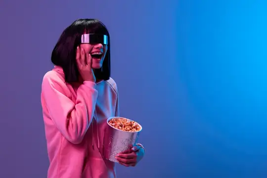 Смеющаяся азиатская девушка в VR-очках с ведром попкорна