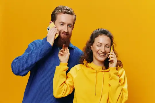 Рыжебородый мужчина и улыбчивая женщина говорят по телефонам на жёлтом фоне