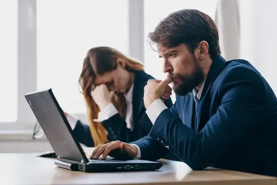 Задумчивый бородатый мужчина в костюме работает за ноутбуком в офисе