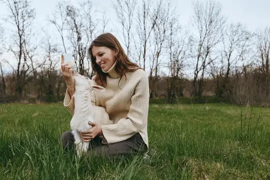 Сцена из жизни: улыбающаяся женщина на открытом воздухе с любопытным козленком, разделяющая нежный момент, воссоединение с природой и животными на открытом лугу при ярком дневном свете