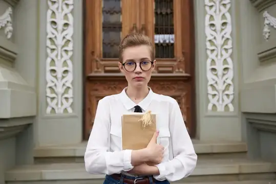 Серьёзная девушка в очках с крафтовым пакетом у старинного здания