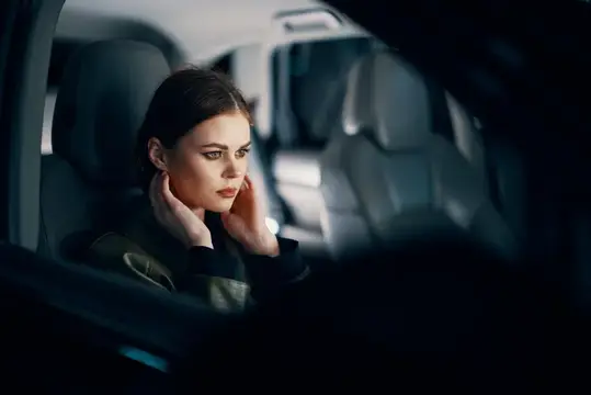 Задумчивая темноволосая женщина сидит в салоне автомобиля