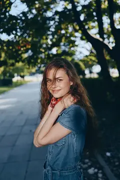 Улыбчивая девушка в джинсовом платье на аллее парка