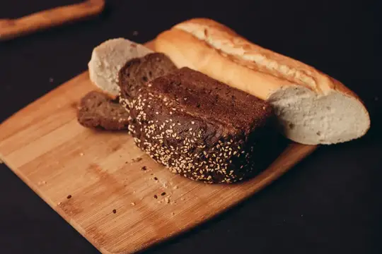 Нарезанный тёмный хлеб с кунжутом и багет на деревянной доске