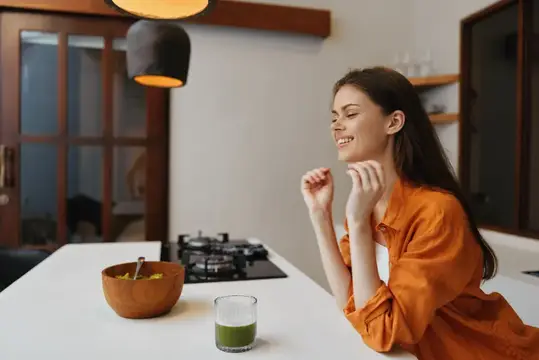 Улыбающаяся темноволосая девушка в оранжевой рубашке на кухне