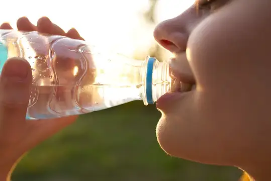 Молодая девушка пьёт воду из бутылки на закате