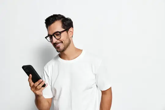 Улыбающийся мужчина в очках смотрит в смартфон на белом фоне