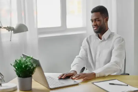 Улыбающийся темнокожий мужчина работает за ноутбуком в светлом офисе