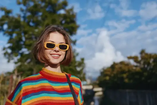 Улыбчивая девушка в жёлтых очках и полосатой футболке на фоне неба